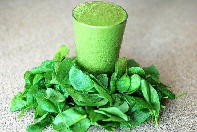 Een glas met een groene smoothie, spinazieblaadjes rondom