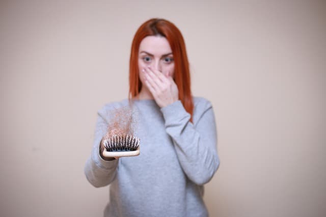 een vrouw kijkt naar een haarborstel vol met haar