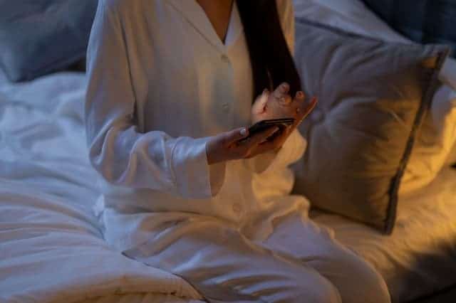 vrouw in pyjama met smartphone in de hand zit op bed