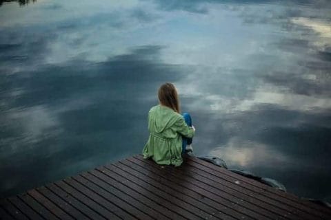  een vrouw zit op de rand van een pier en kijkt in het water