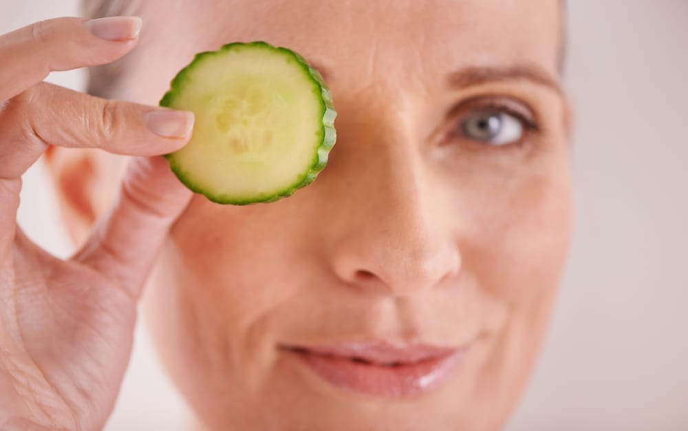  Een vrouw houdt een schijfje komkommer tegen haar oog
